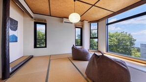 A tatami mat room with large windows, a hanging light fixture, and a view of trees and buildings. - Glampetit Horizon (Atami)