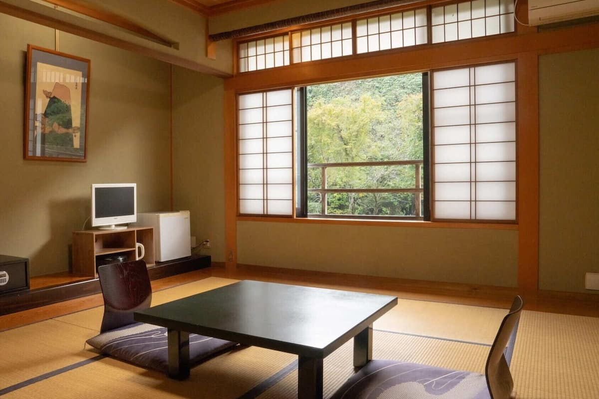 A traditional Japanese room with tatami flooring, a low table, a television, and a refrigerator.