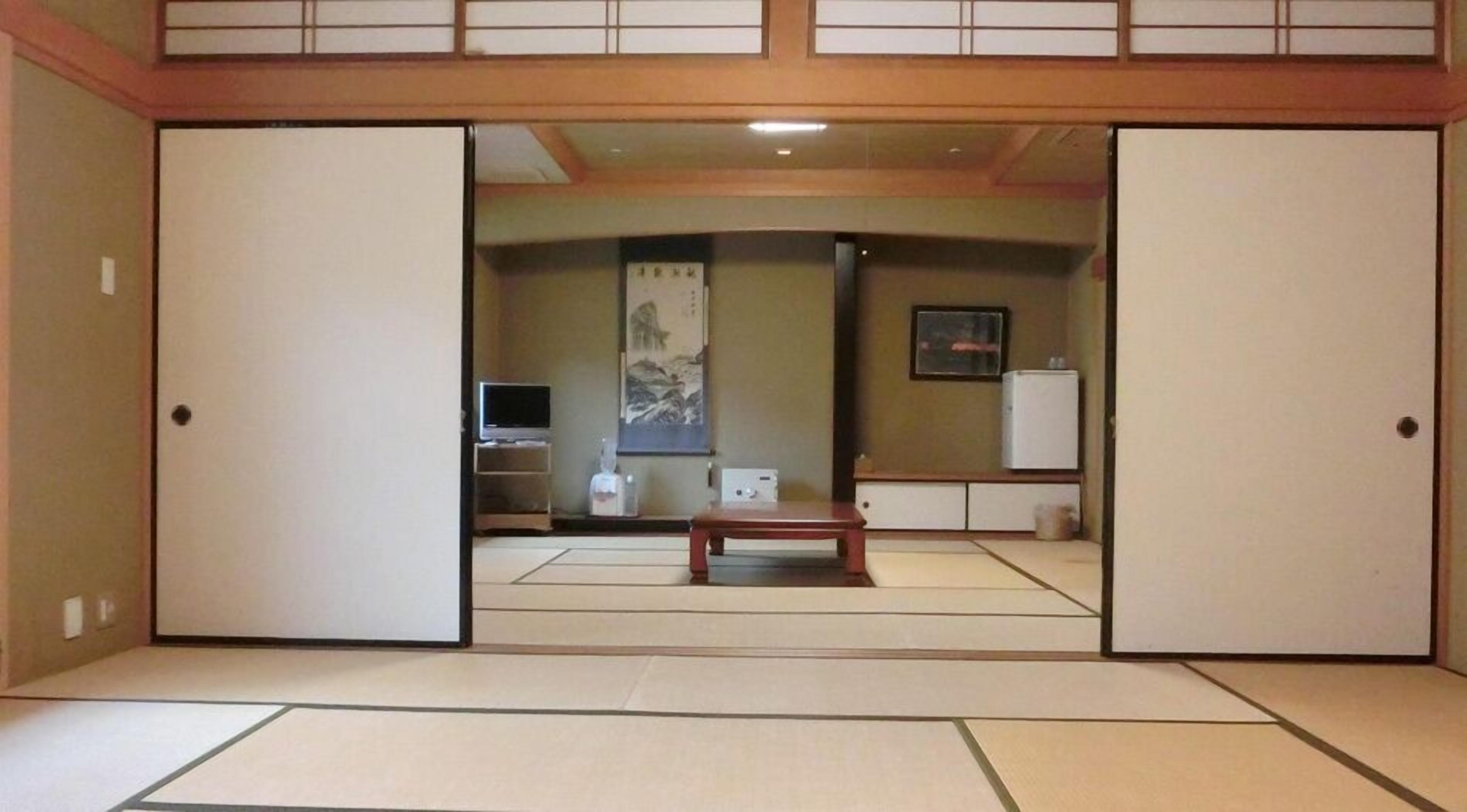 A traditional Japanese room with tatami flooring, a television, a refrigerator, and a painting on the wall.