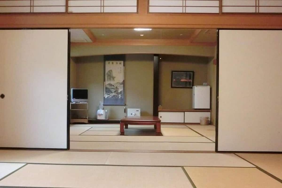 A traditional Japanese room with tatami flooring, a television, a refrigerator, and a painting on the wall.