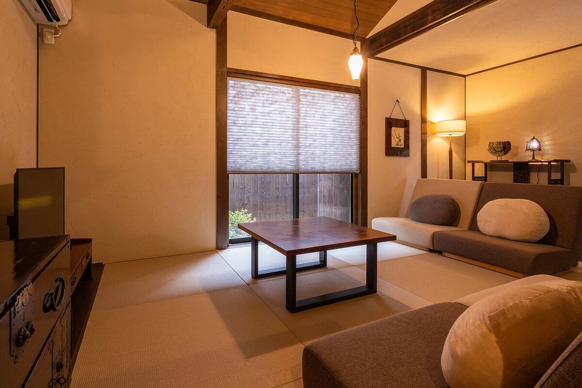 Un salon avec un sol recouvert de tatamis, un canapé, une table basse et un téléviseur.