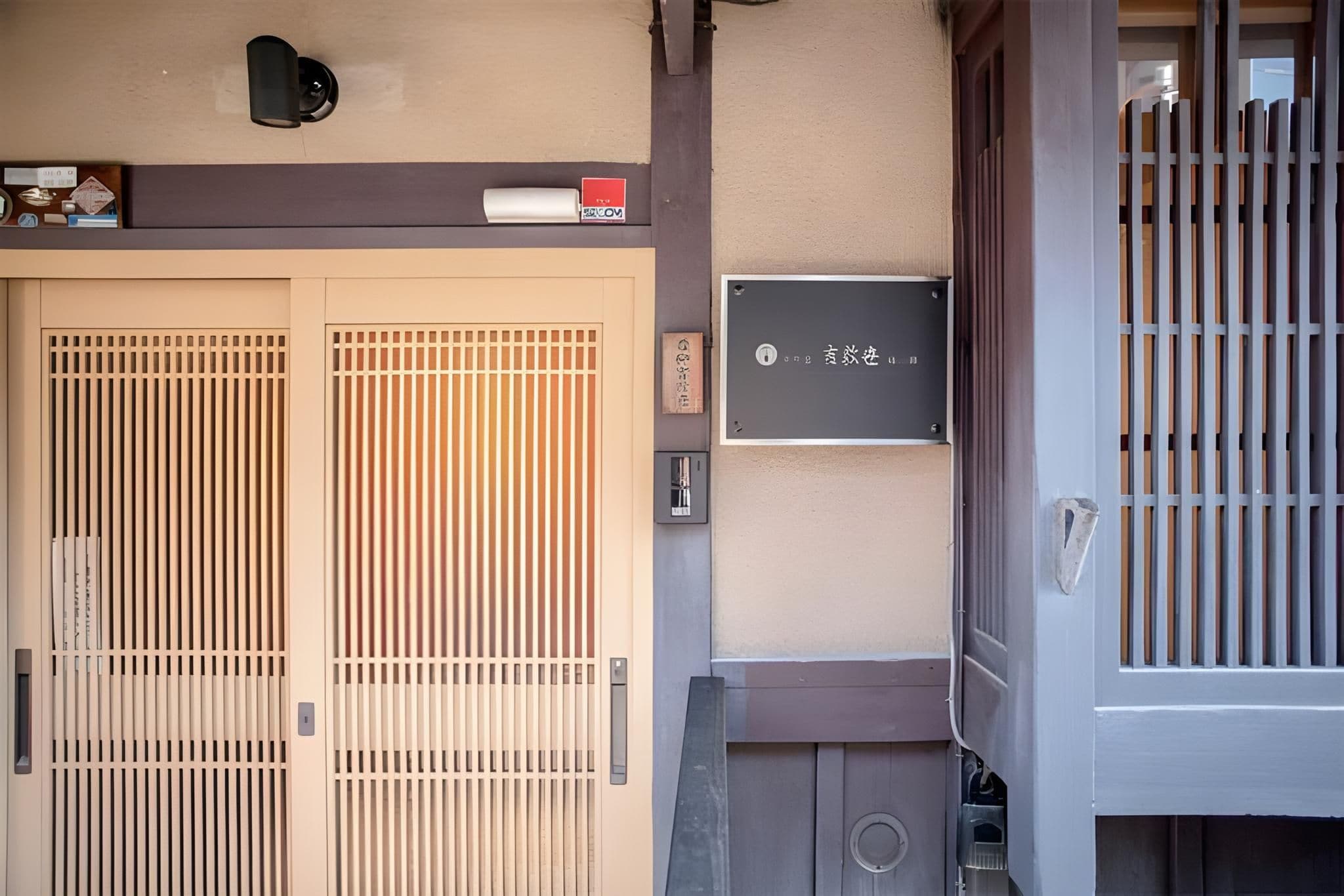 A traditional Japanese gate with sliding doors, a small sign with Japanese characters, and a wall-mounted mailbox.