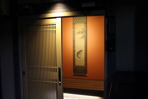 Ett traditionellt japanskt rum med en skjutdörr, ett inramat konstverk på väggen och en träpaneldesign.