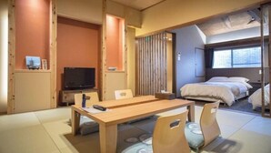 Perinteinen japanilaistyylinen huone, jossa on tatamimatto, puinen ruokapöytä, televisio ja sängystä avautuva näkymä.
