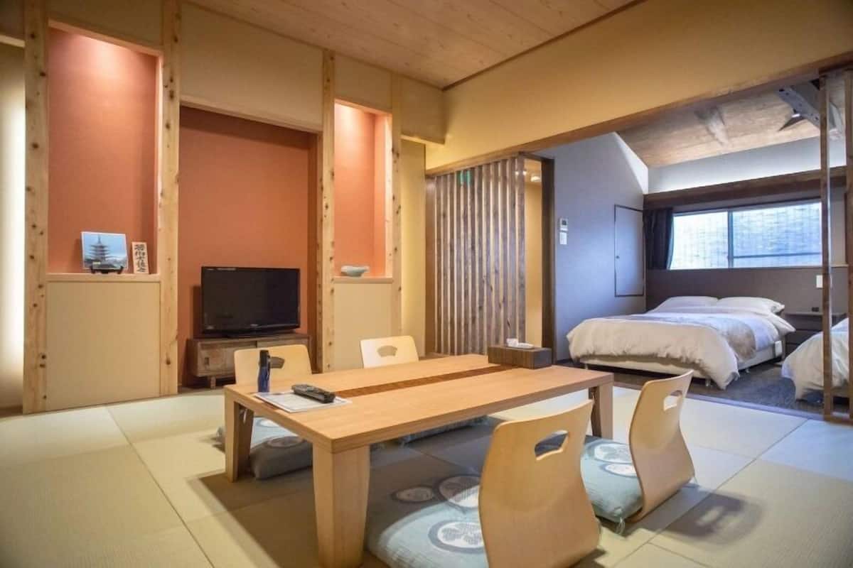 A traditional Japanese-style room with tatami flooring, a wooden dining table, a television, and a bed with a window view.