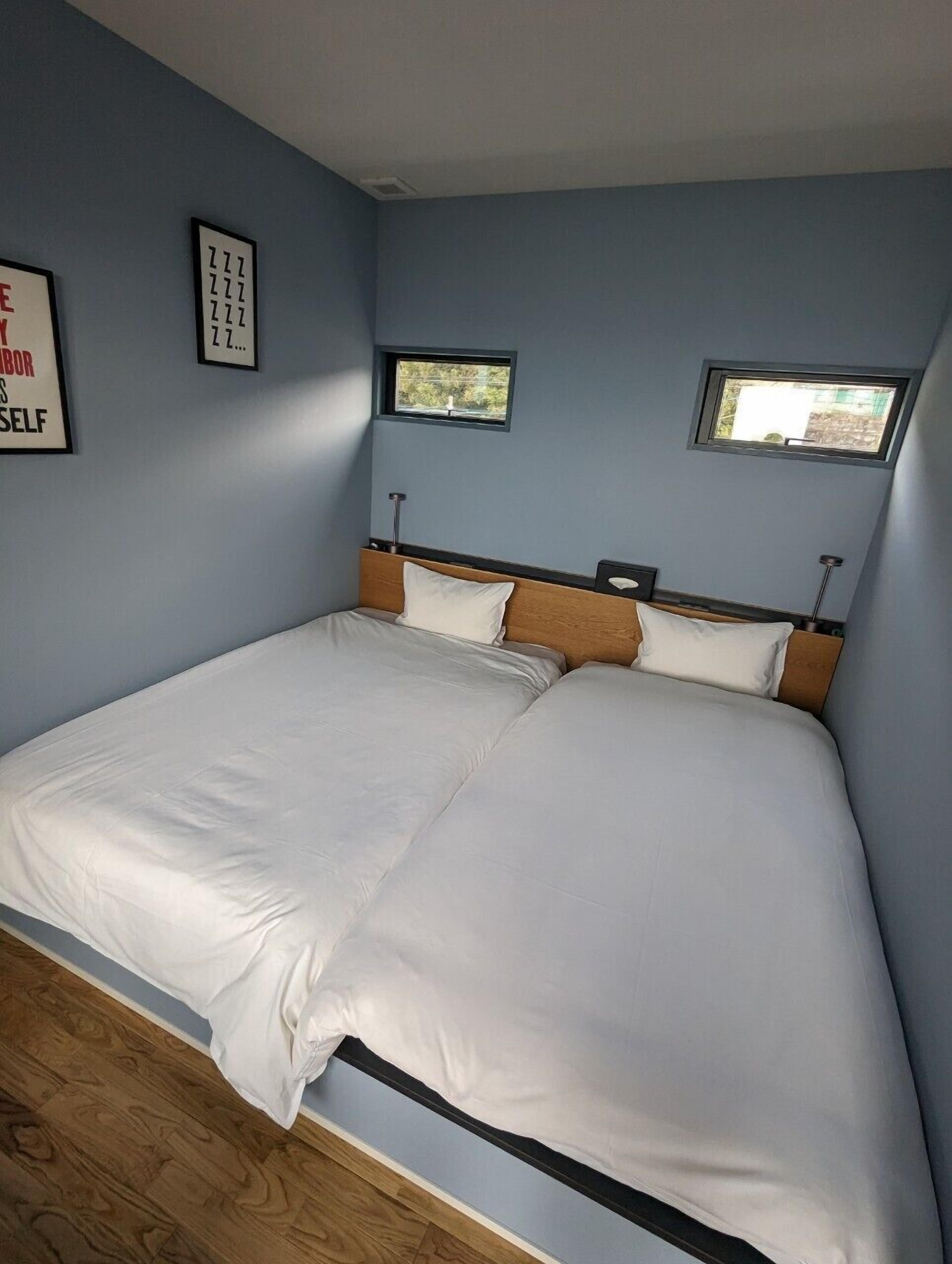 A bedroom with a large bed, two windows, and a wall-mounted light fixture.
