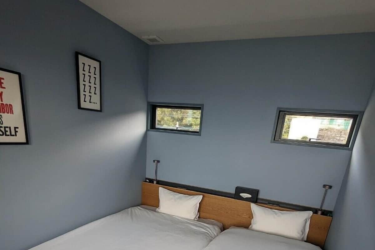 Une chambre à coucher avec un grand lit, deux fenêtres et un luminaire fixé au mur.