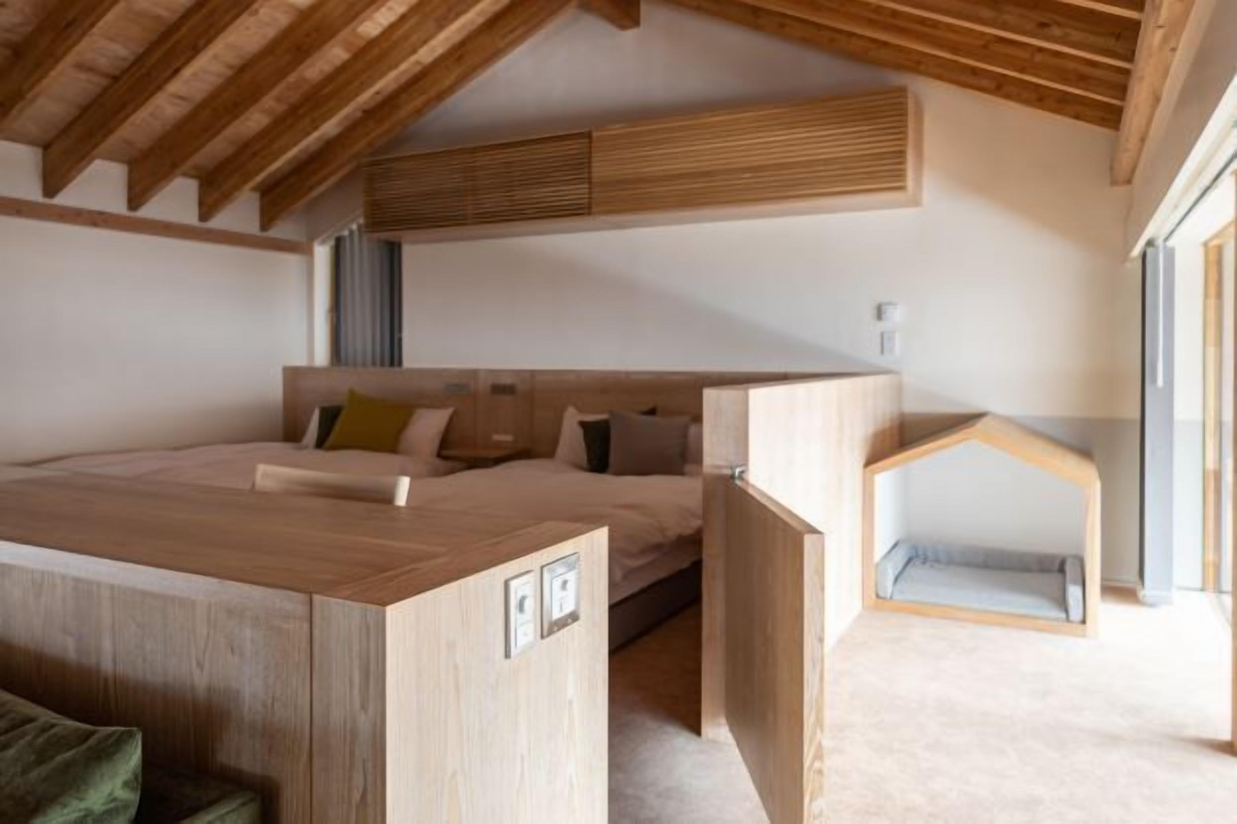 A bedroom with a wooden ceiling, a bed, a desk, and a small child bed.
