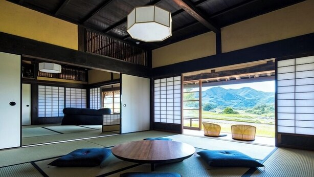 Een traditionele Japanse kamer met tatami vloeren, een lage tafel, kussens, schuifdeuren en uitzicht op bergen.