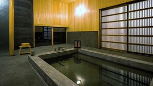 Een traditionele Japanse kamer met tatami vloerbedekking, een klein houten krukje, een stenen lantaarn en een verschuifbaar shoji scherm.