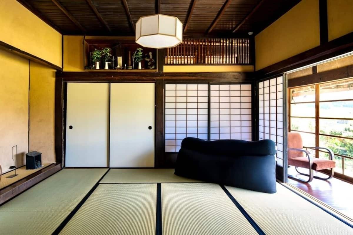A traditional Japanese room with tatami flooring, a black sofa, a hanging lamp, and a view through a shoji screen.