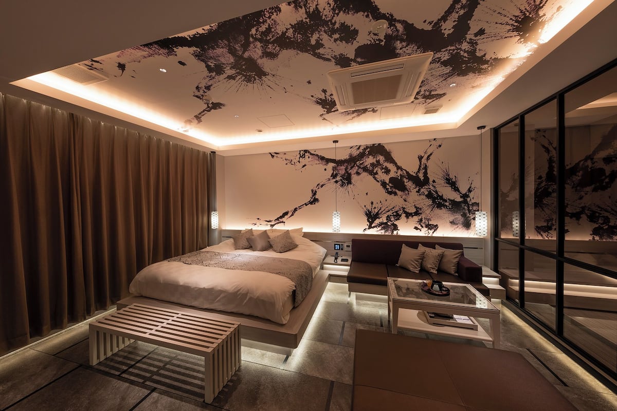A modern bedroom with a large bed, a sofa, a coffee table, and a ceiling with a unique black and white design.