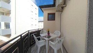 A balcony with a table and chairs, a small window, and a building in the background. - A few Steps From the Beach in Lignano With Balcony (Lignano Sabbiadoro)