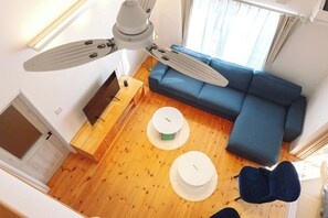Una sala de estar moderna con un sofá azul, dos mesas redondas blancas, un ventilador de techo y suelo de madera.