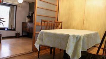 A dining area with a table covered by a patterned tablecloth, wooden chairs, and a sliding door in the background.