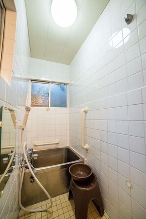 Ett badrum med vita kakelväggar, ett fönster, ett handfat, en toalett och en dusch.