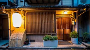 A traditional Japanese entrance with a wooden gate, a sliding door, and a small wooden structure to the left.