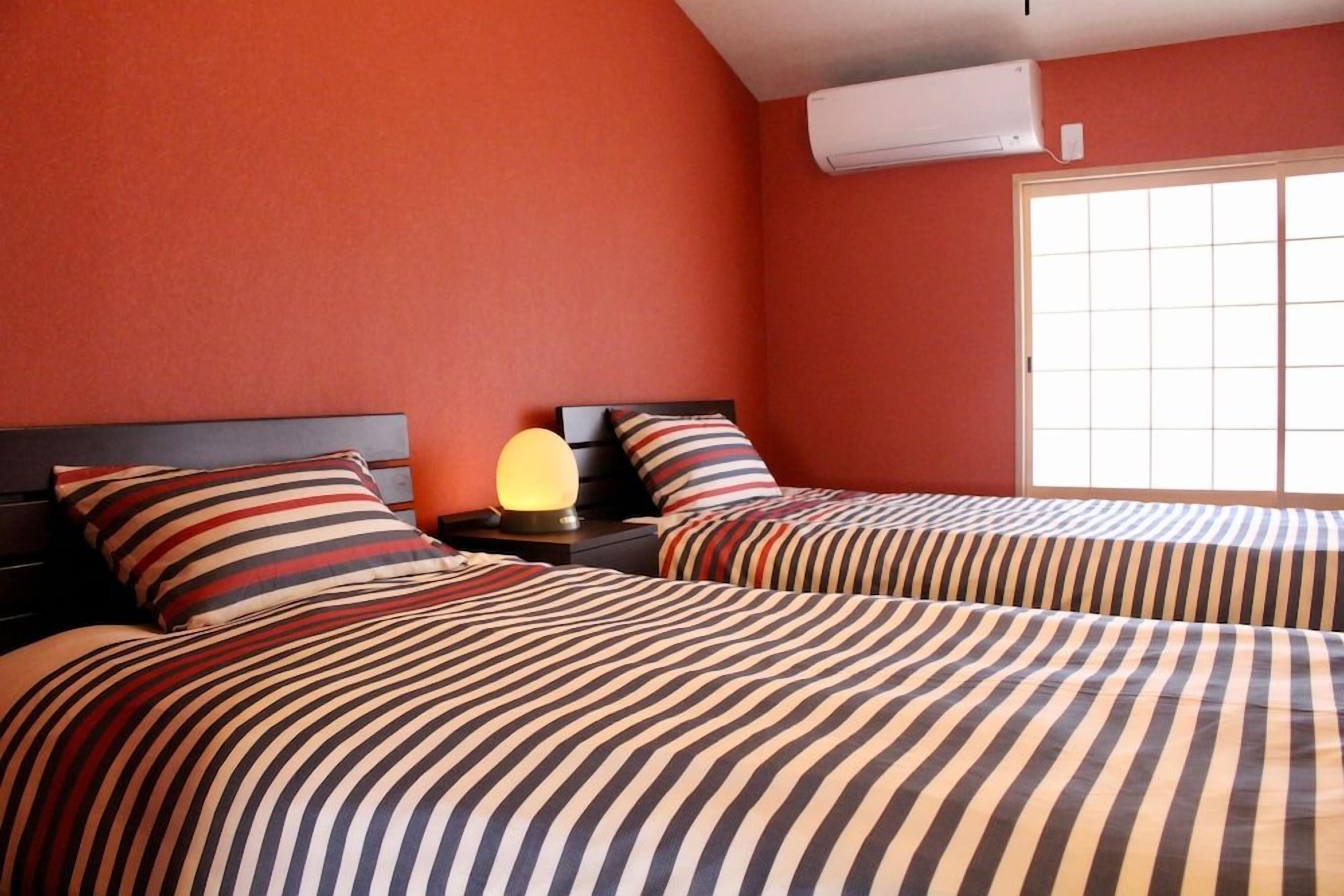 A hotel room with two beds, striped bedding, a bedside lamp, and a window with blinds.