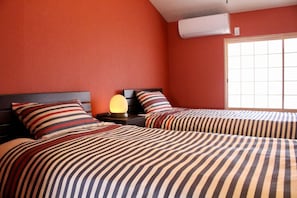 A hotel room with two beds, striped bedding, a bedside lamp, and a window with blinds. - Kyoto Kumano House (Kyoto)