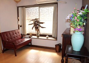 A room with a sofa, a window with curtains, a vase with flowers, and a small table. - Kyoto Kumano House (Kyoto)