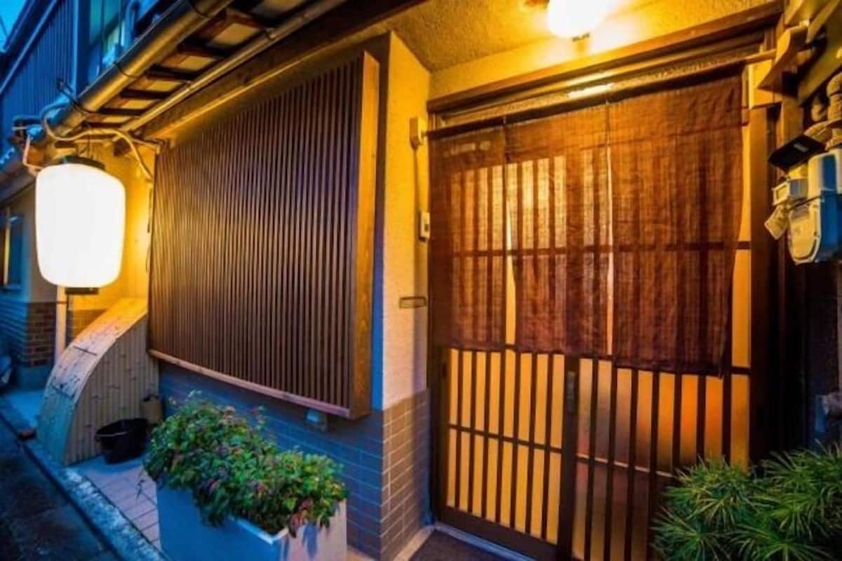 A traditional Japanese-style building with a wooden gate, a lantern, and potted plants.