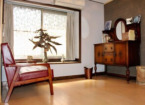 A room with a wooden floor, a red leather chair, a wooden cabinet with books, and a window with curtains. - Kyoto Kumano House (Kyoto)