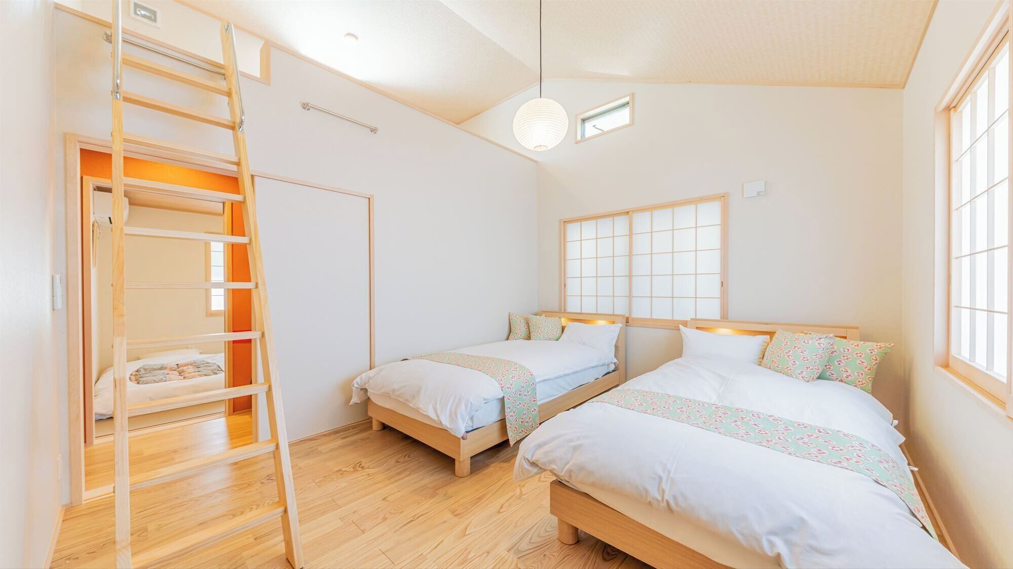 A room with two beds, a ladder, a window with a view, and a light fixture.