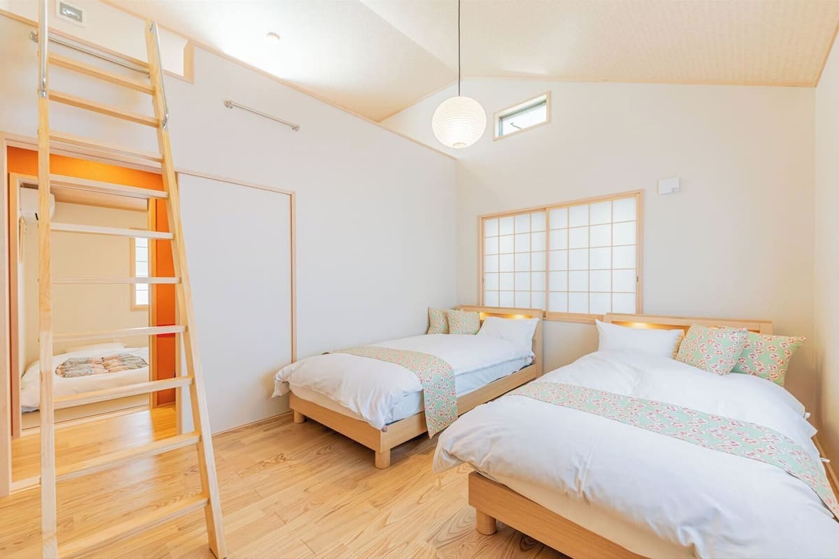 Une chambre avec deux lits, une échelle, une fenêtre donnant sur un beau paysage et un luminaire.