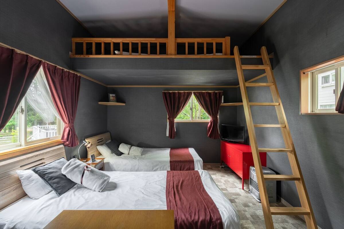 A room with bunk beds, a TV, a ladder, and a window with curtains.