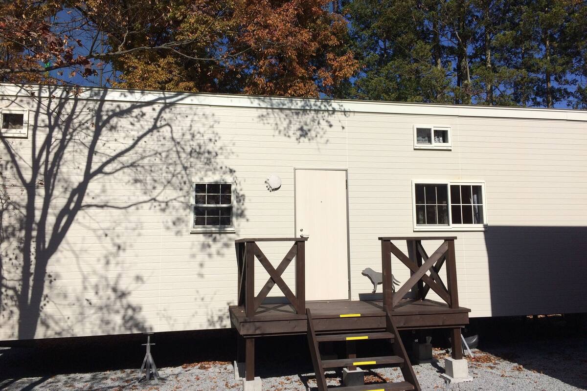 A white mobile home with a small porch, a door, and two windows.
