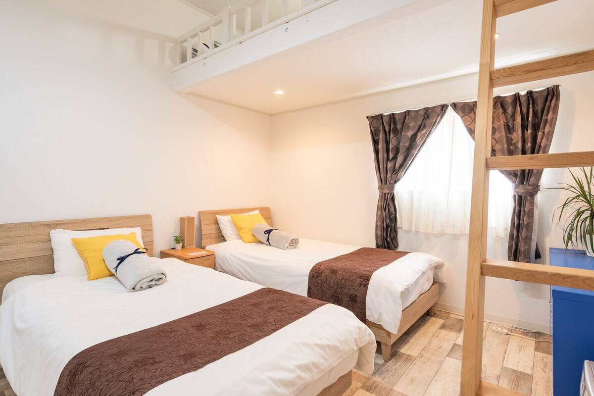 A hotel room with two beds, a wooden headboard, a nightstand, a potted plant, and a window with curtains.