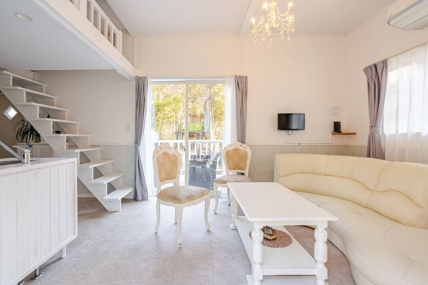 Een moderne woonkamer met een bank, fauteuils, een televisie, een trap en een balkon.