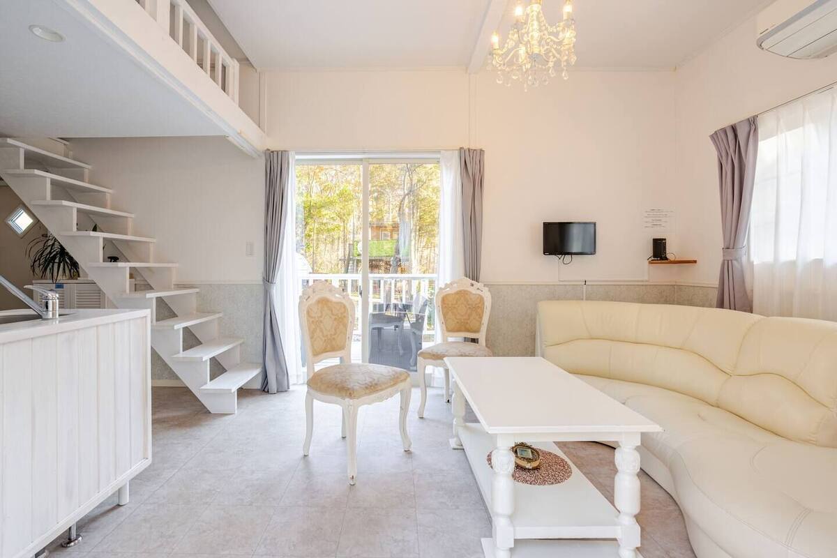 A modern living room with a sofa, chairs, a TV, a staircase, and a balcony.