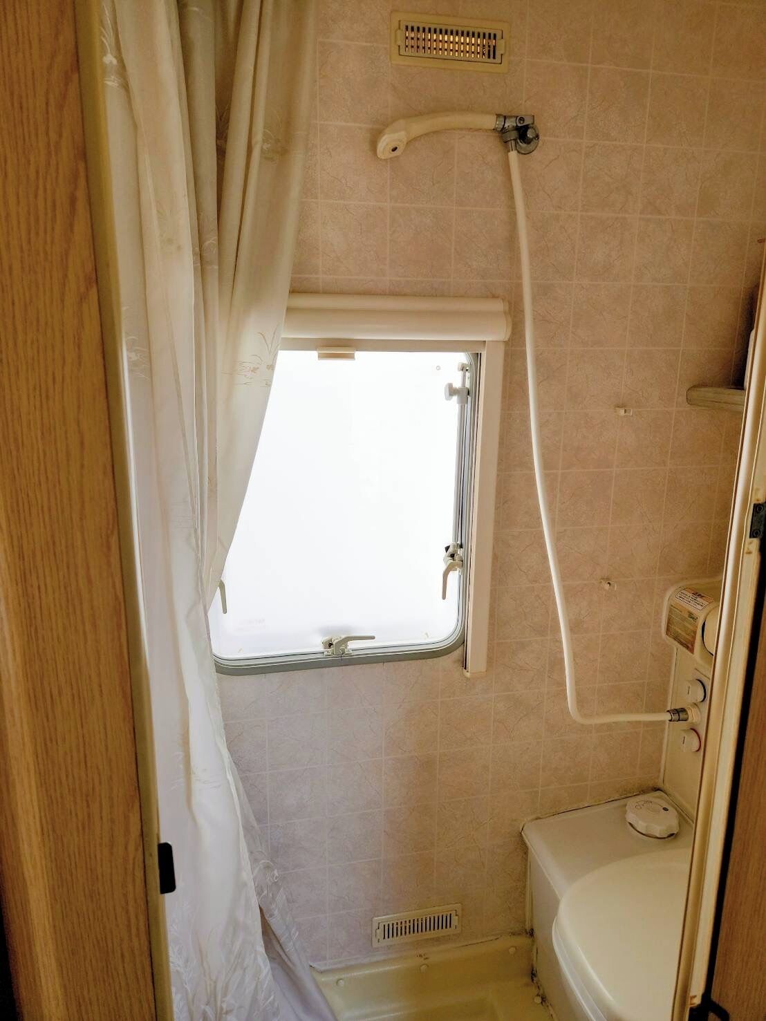 Een kleine badkamer met raam, douche en toilet.