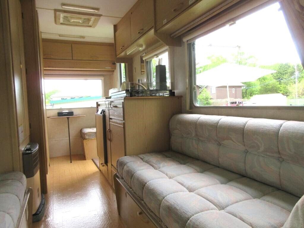 Ein kompaktes Wohnmobil-Interieur mit einer Küchenzeile, einer gepolsterten Sitzgruppe und einem Fenster mit Blick ins Freie.