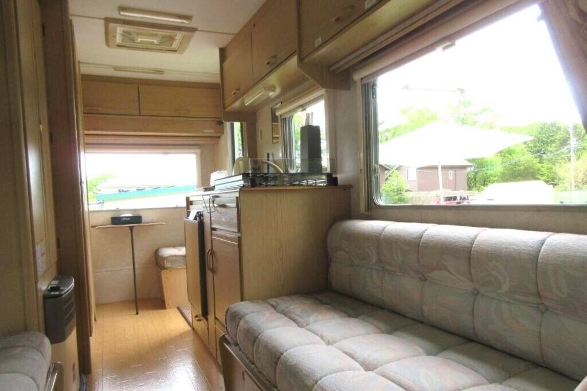 A compact RV interior with a kitchenette, a cushioned seating area, and a window providing a view of the outdoors.