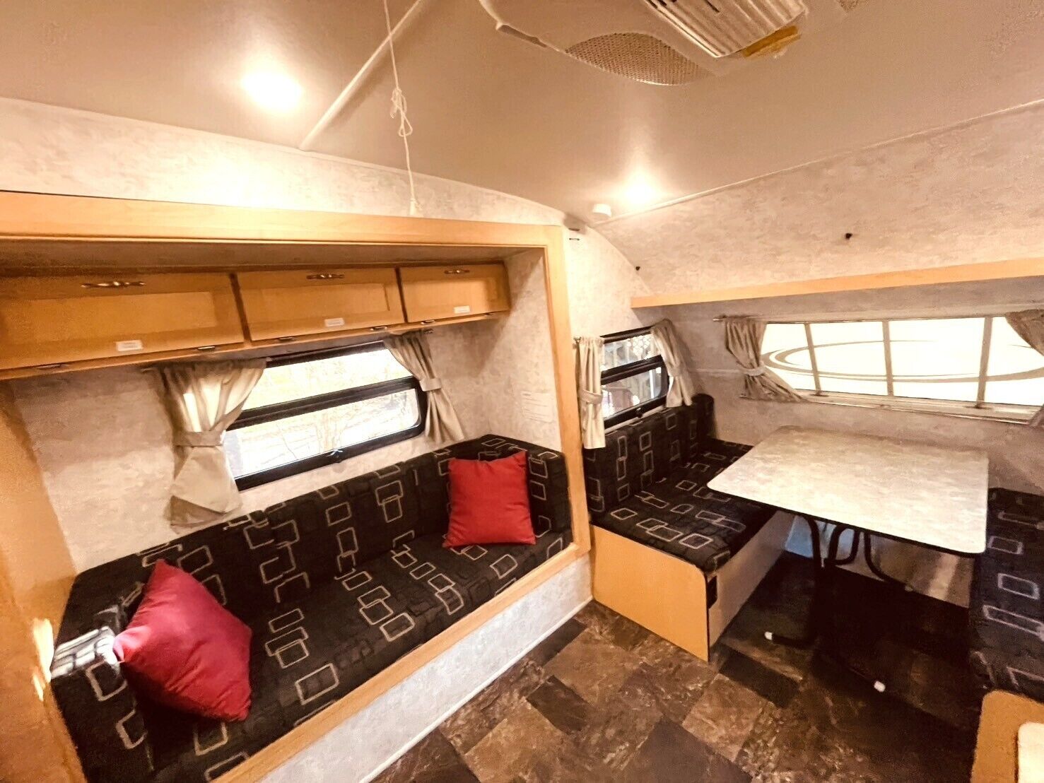 Ein kompaktes Wohnmobil-Interieur mit einer Küchenzeile, einer Sitzecke mit Kissen und einem Fenster, das natürliches Licht hereinlässt.