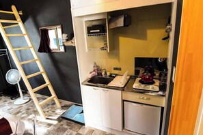 A compact kitchen with a sink, stove, and cabinets, a ladder, and a fan. - Trailer House Hotel Jennie (Miyota)