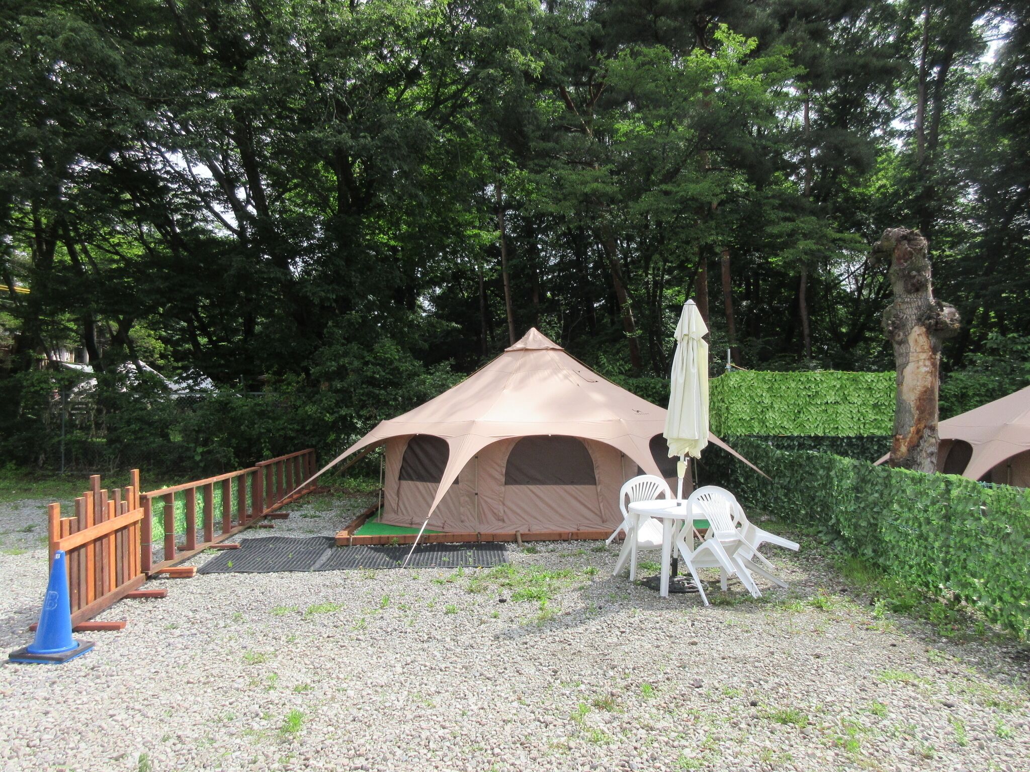 Een camping met een tent, een tafel met stoelen en een blauwe verkeerspaal.