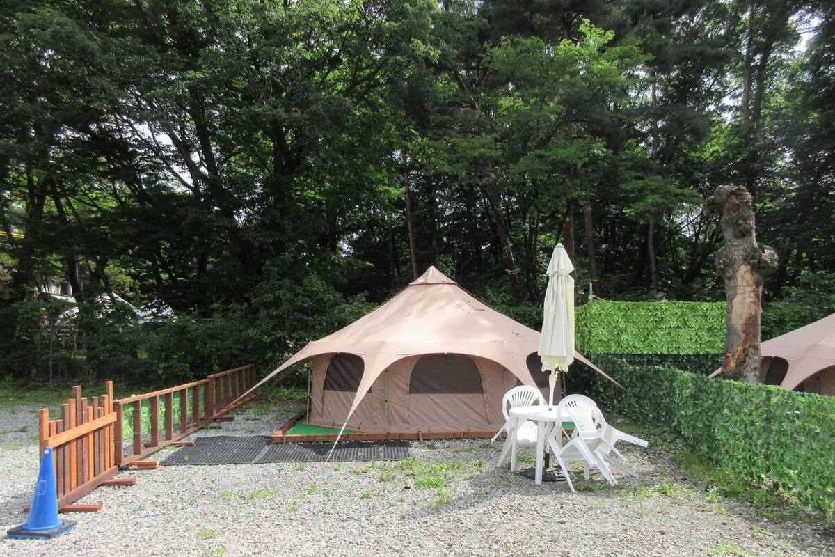 A camping site with a tent, a table with chairs, and a blue traffic cone.