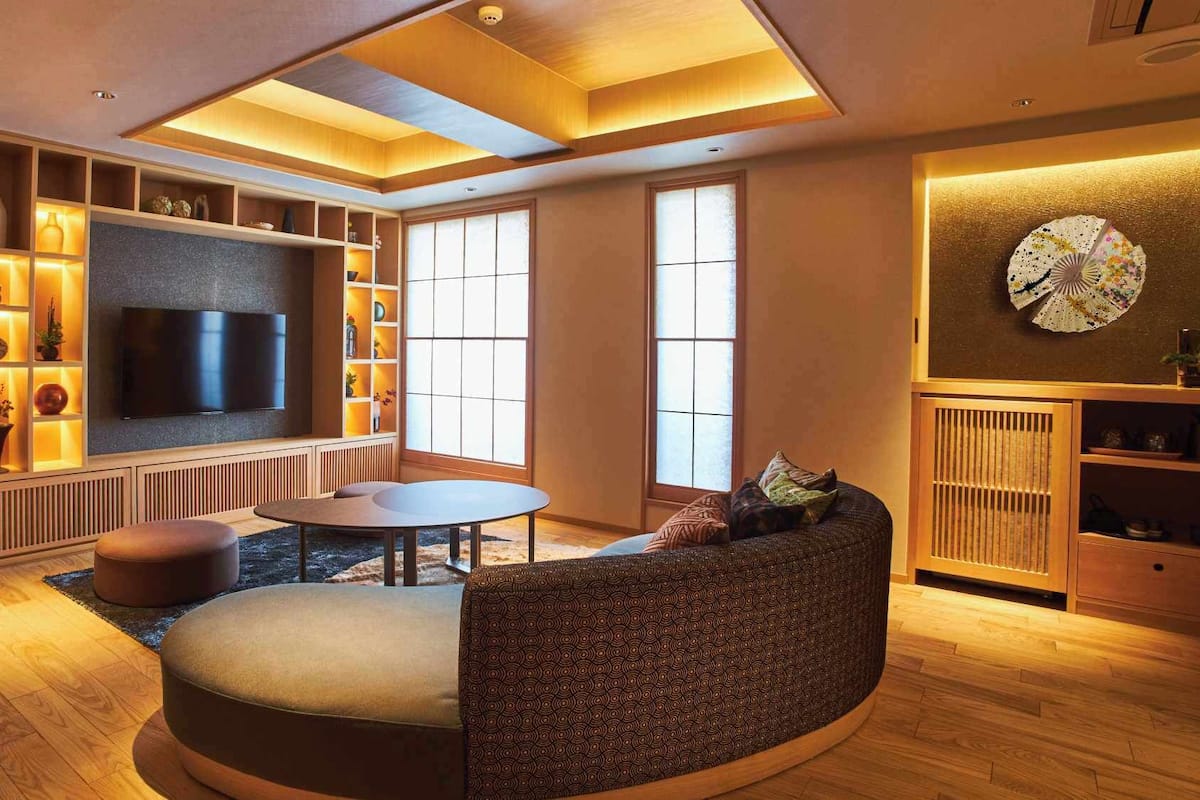 Ein modernes Wohnzimmer mit Fernseher, Sitzgelegenheiten und einem großen Fenster.