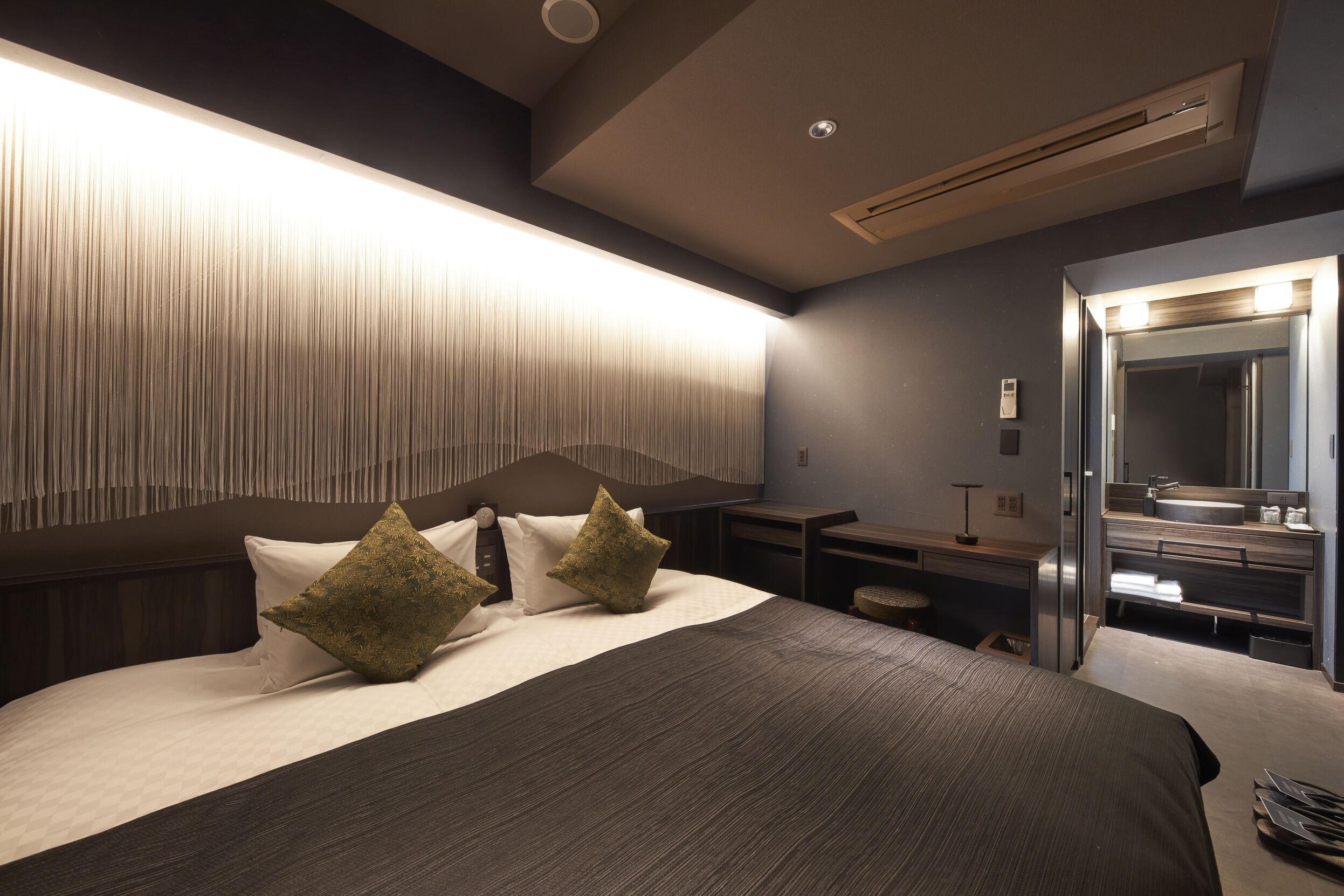 A modern hotel room with a large bed, bedside tables, a mirror, and a built-in air conditioning unit.