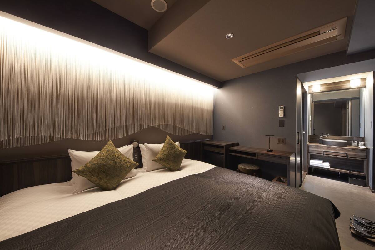 A modern hotel room with a large bed, bedside tables, a mirror, and a built-in air conditioning unit.