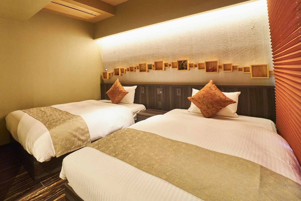 A hotel room with two beds, a wooden headboard, a textured wall, and a ceiling light.