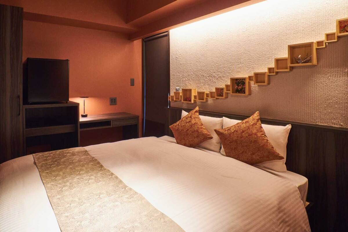 A hotel room with a bed, a desk, a television, and a wall with a textured pattern and wooden shelves.