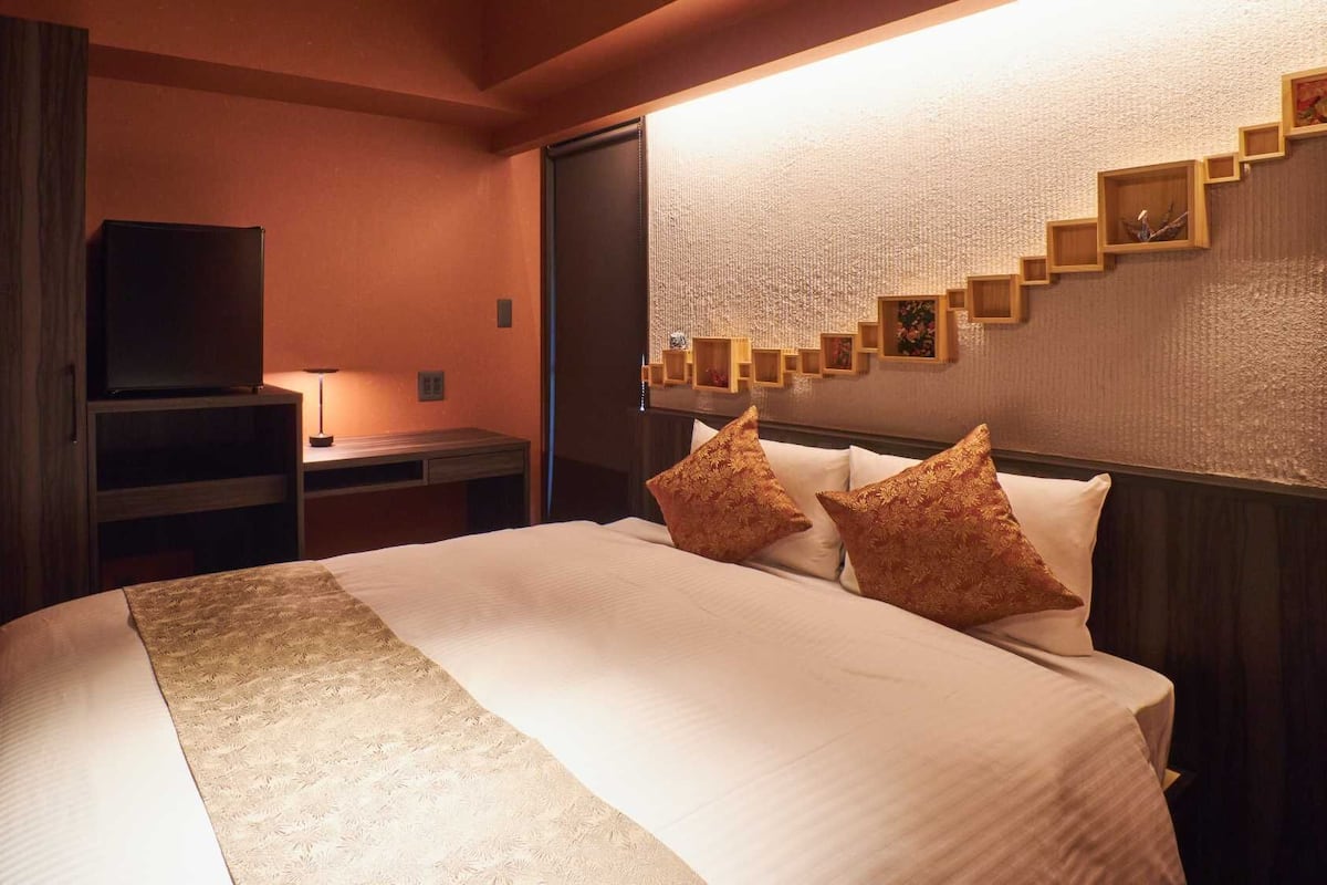 Ein Hotelzimmer mit einem Bett, einem Schreibtisch, einem Fernseher und einer Wand mit strukturierter Musterung und Holzregalen.