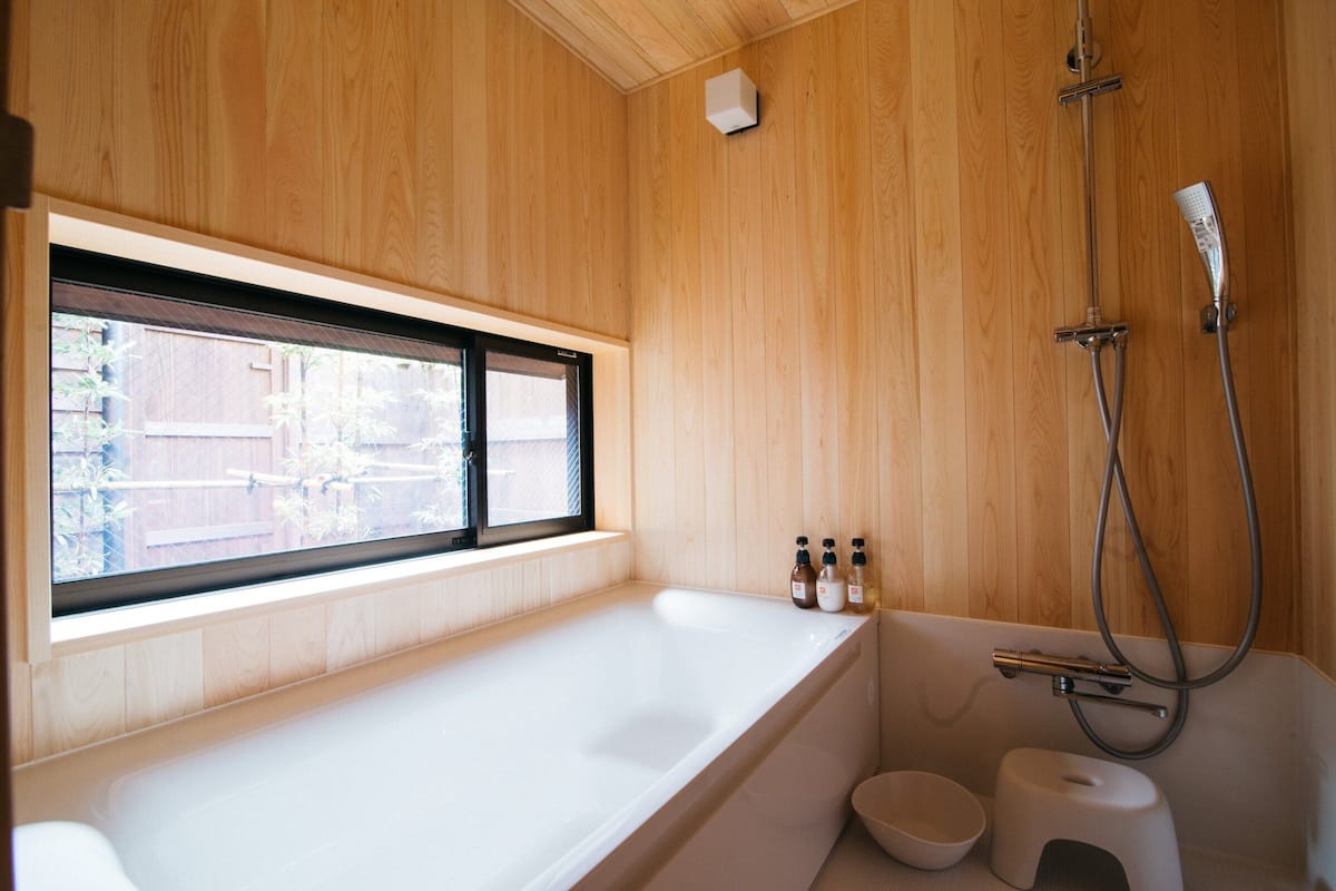 A modern bathroom with a wooden interior, a large bathtub, a window, and a shower.