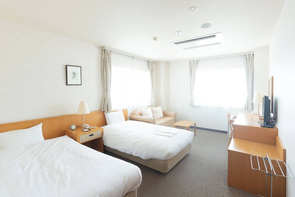 A hotel room with two beds, a desk, a chair, a TV, and a window with curtains.