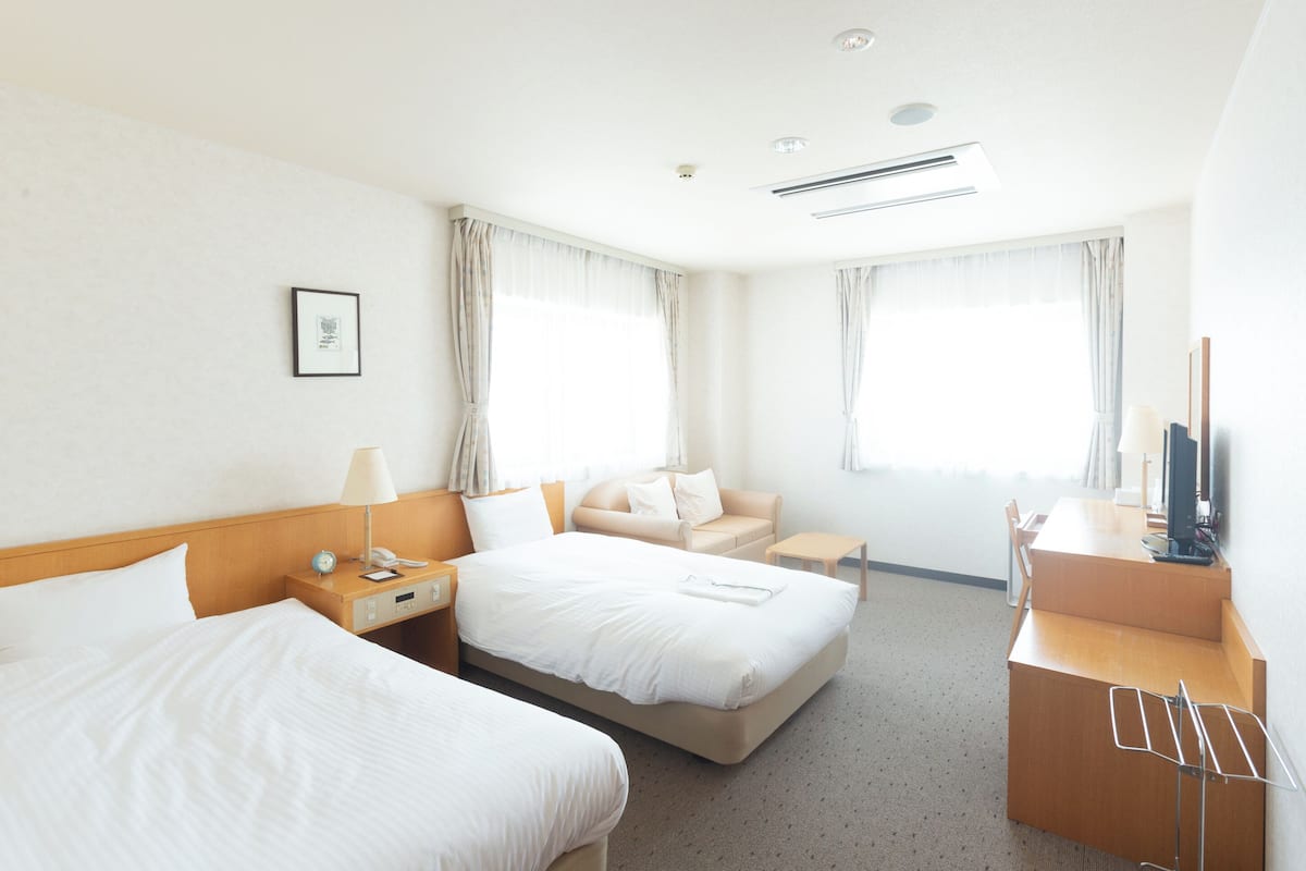 A hotel room with two beds, a desk, a chair, a TV, and a window with curtains.