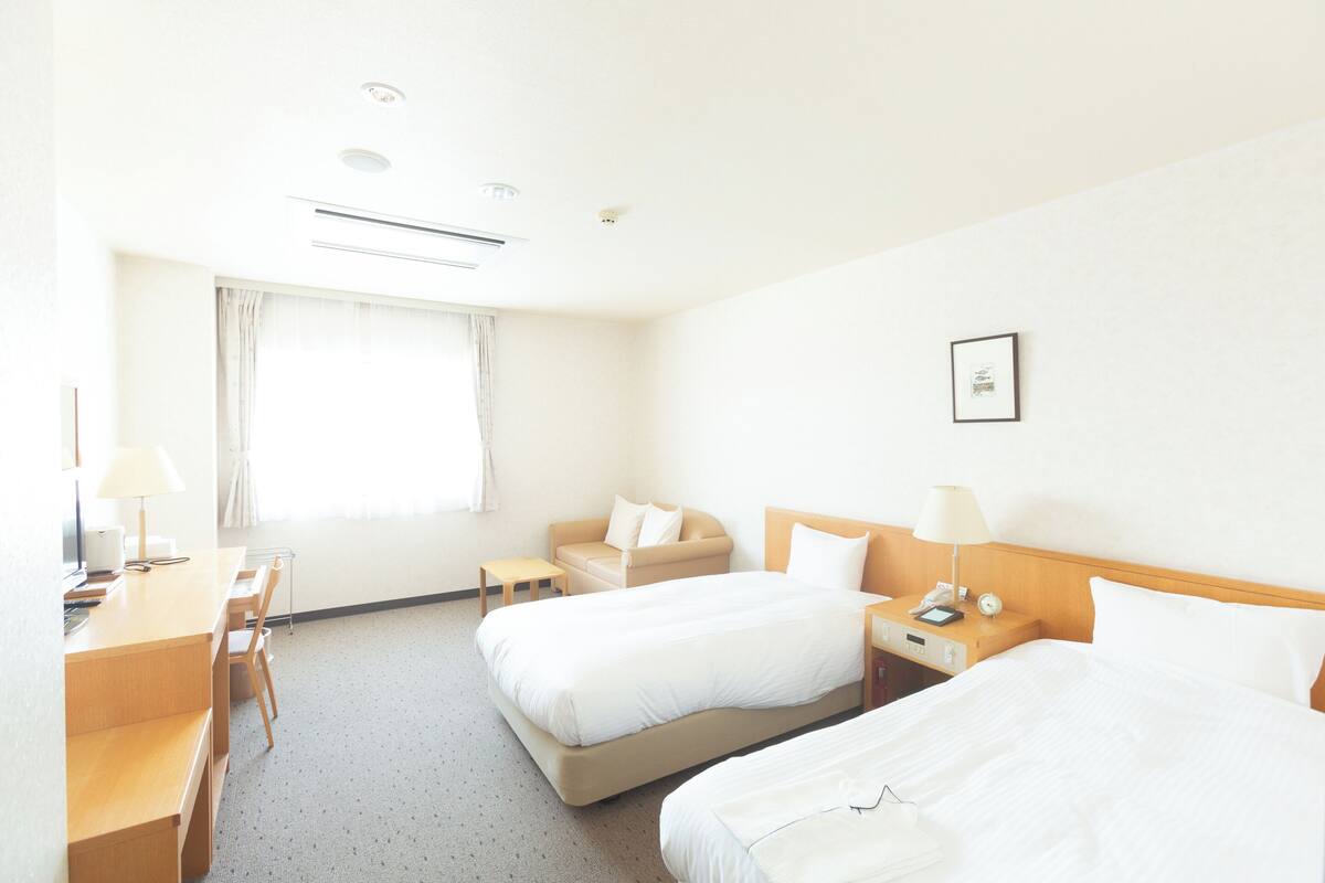 A hotel room with two beds, a desk, a chair, a small table, and a window with curtains.